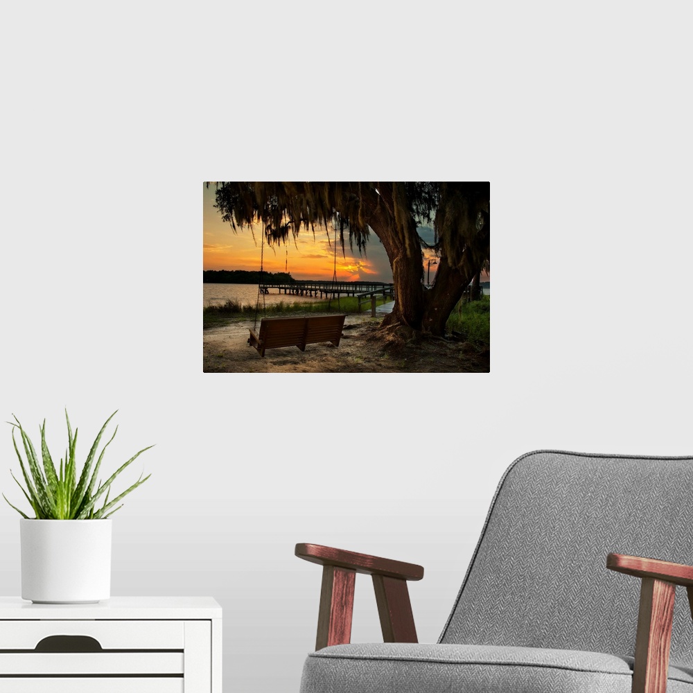 A modern room featuring A vibrant photograph of bench swing tethered to a dropping tree, looking out over a lake at sunset.