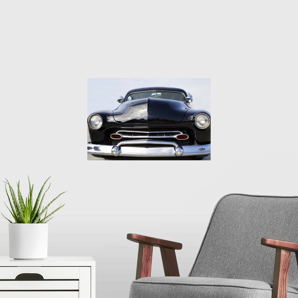 A modern room featuring The front of a classic car with a chrome bumper and dark paint.