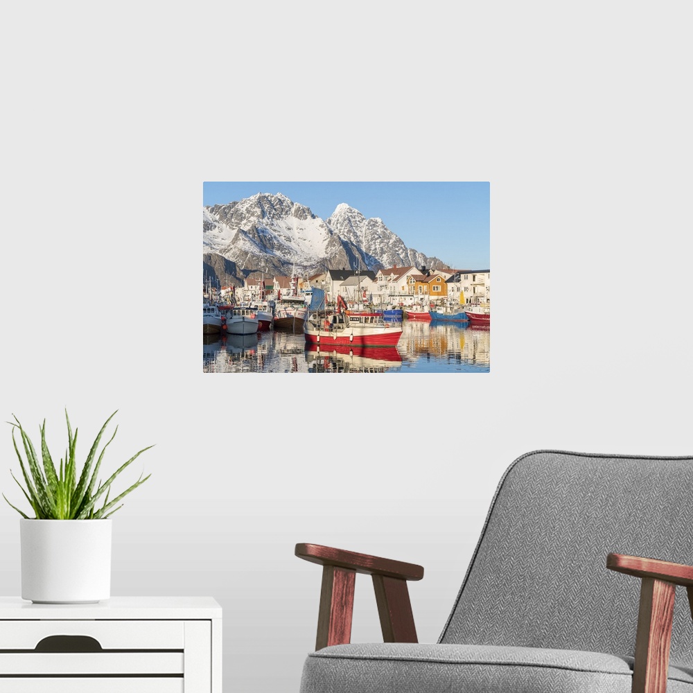 A modern room featuring Fishing boats in the harbour, with snowcapped mountains in the background. Henningsvaer, Nordland...