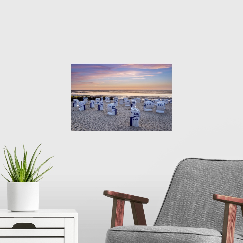A modern room featuring Duhnen, Cuxhaven, Lower Saxony, Germany. Strandkorb beach chairs and the Wadden Sea at sunset.