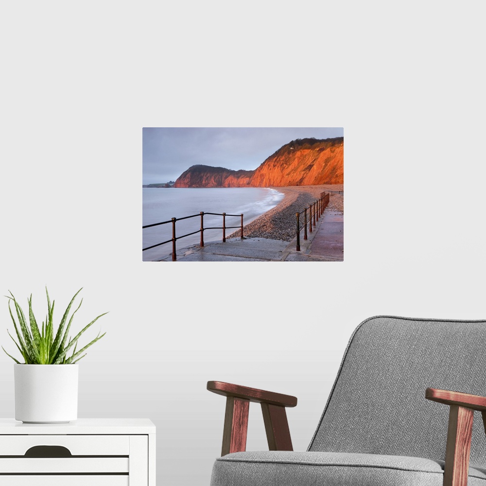 A modern room featuring Early morning sunlight glows against the distinctive red cliffs of High Peak, viewed from the bea...