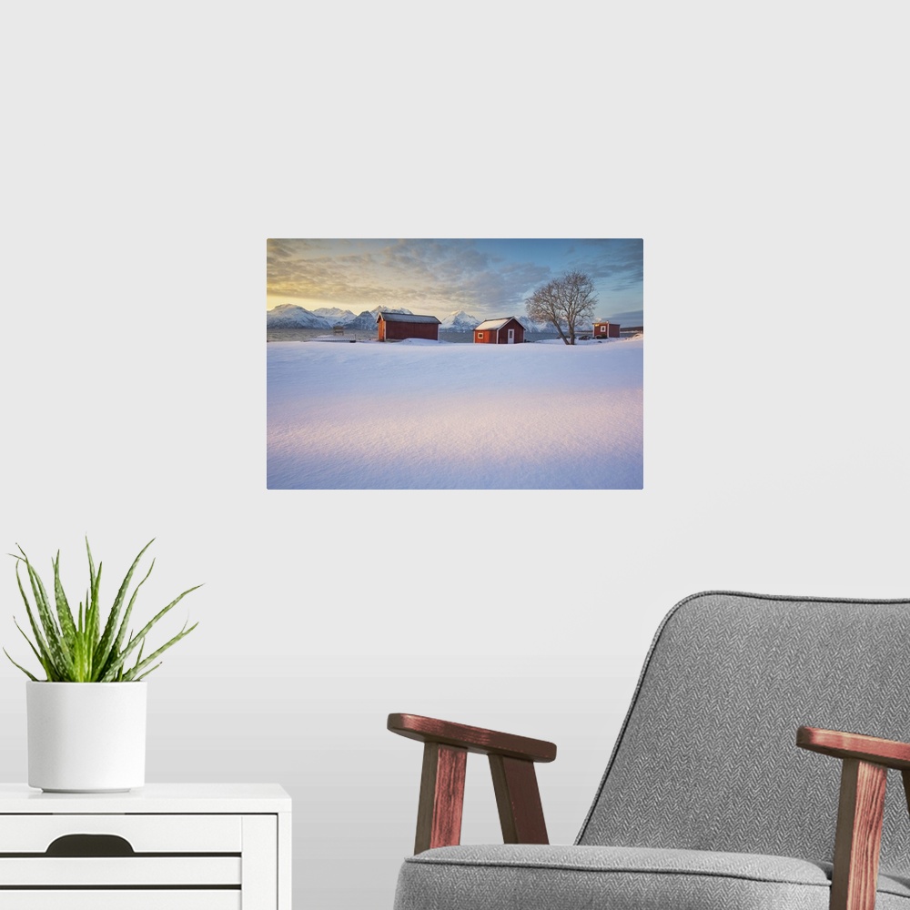 A modern room featuring The orange sky at sunset frame the frozen sea and typical Rorbu immersed in the snow Djupvik Lyng...