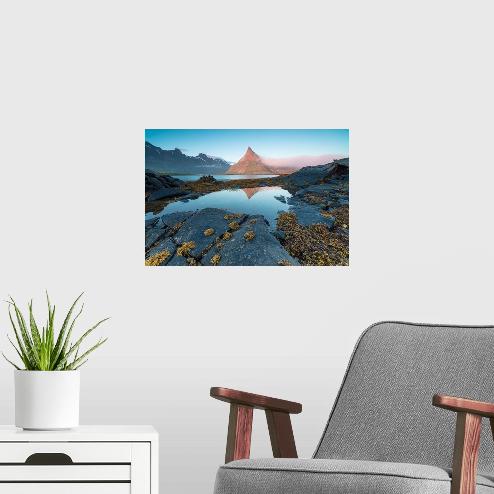 A modern room featuring The rocky peak of Volanstinden lighted up by the midnight sun is reflected in blue sea Fredvang L...