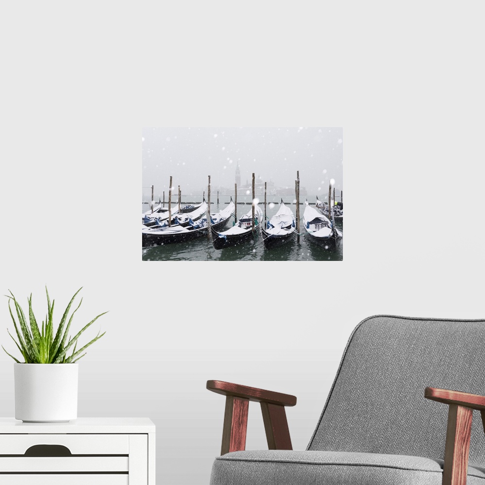 A modern room featuring Winter snowfall in the city of Venice, gondolas covered by snow and in the background the San Gio...