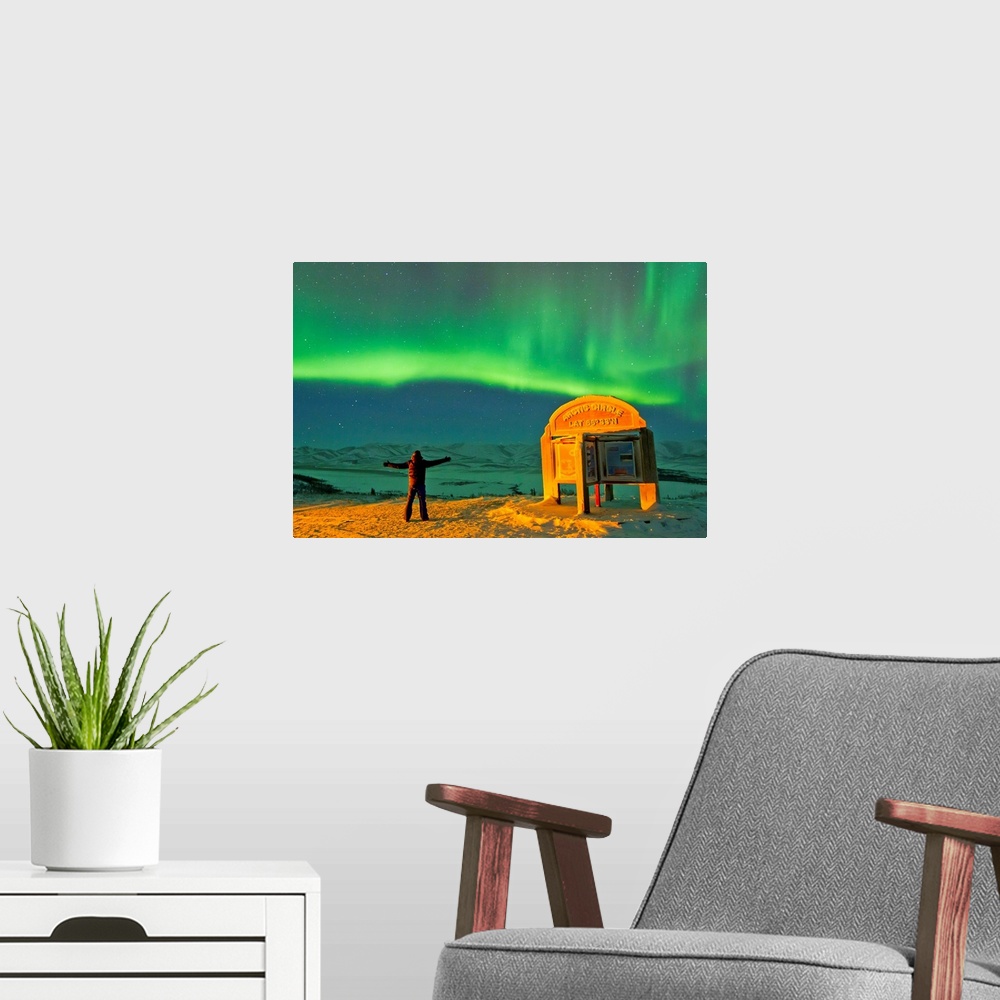 A modern room featuring A man looks in awe at the northern lights near the Arctic Circle sign.
