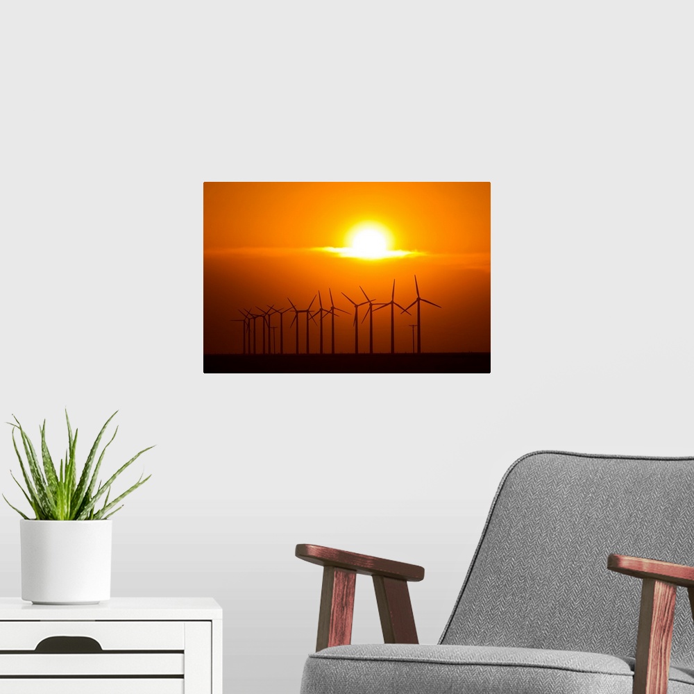 A modern room featuring The sun sets behind a row of spinning windmills or wind turbines.