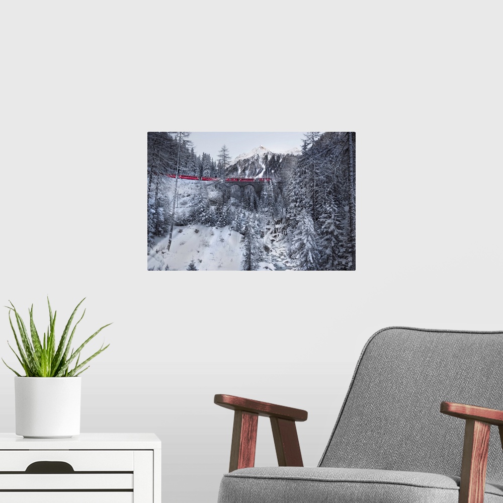 A modern room featuring Photograph of a red train passing through a snowy mountainous valley in winter along an arched ra...