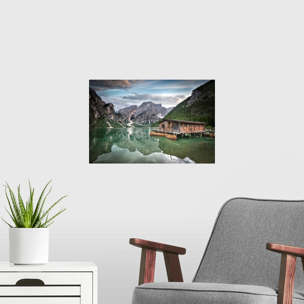 A modern room featuring Jade green lake reflecting mountainous valley and cabin.