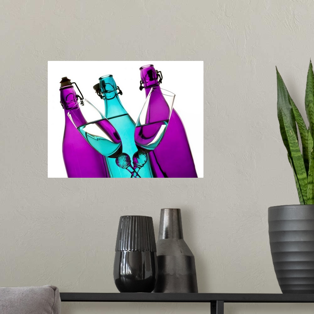 A modern room featuring turquoise and purple glass bottles with two champagne flutes crossing in front on a white backgro...