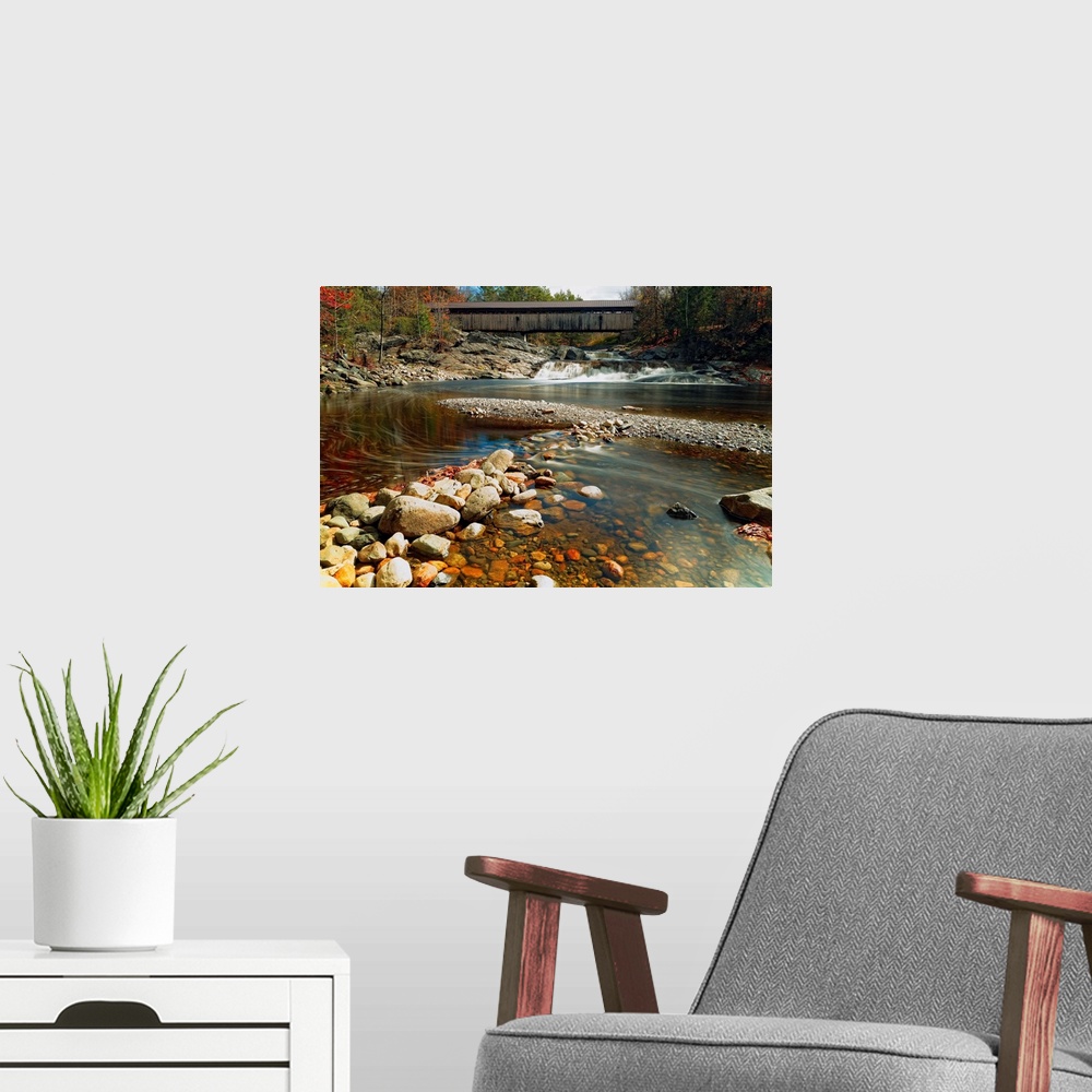 A modern room featuring A rocky riverbed in New Hampshire with the Swiftwater Covered Bridge in the distance.
