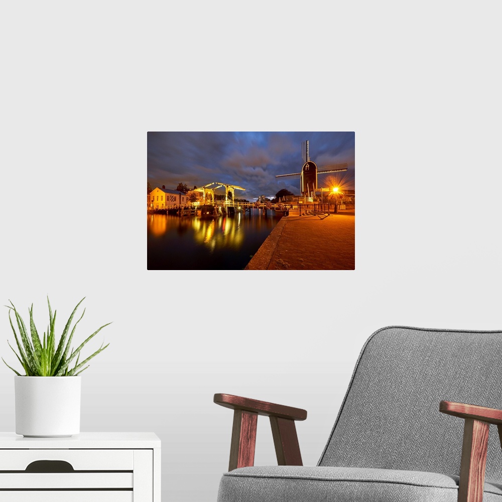 A modern room featuring View of a canal with a small bridge and windmill at night, Leiden, South Holland, Netherlands.