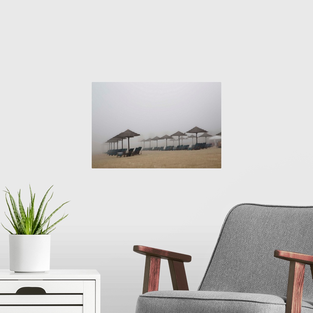 A modern room featuring Blurred photograph of a sandy beach lined with beach chairs and umbrellas, created with multiple ...