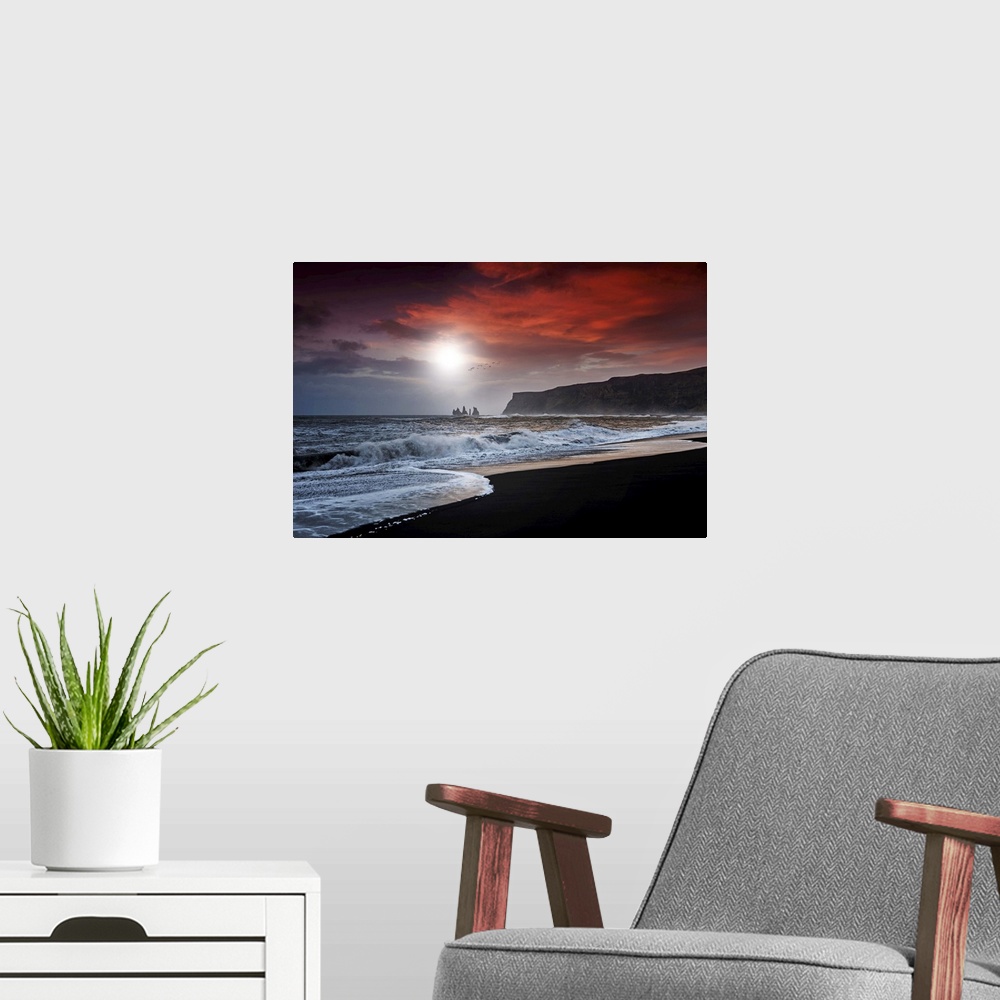 A modern room featuring A photograph of a dark coastline under a red clouds.