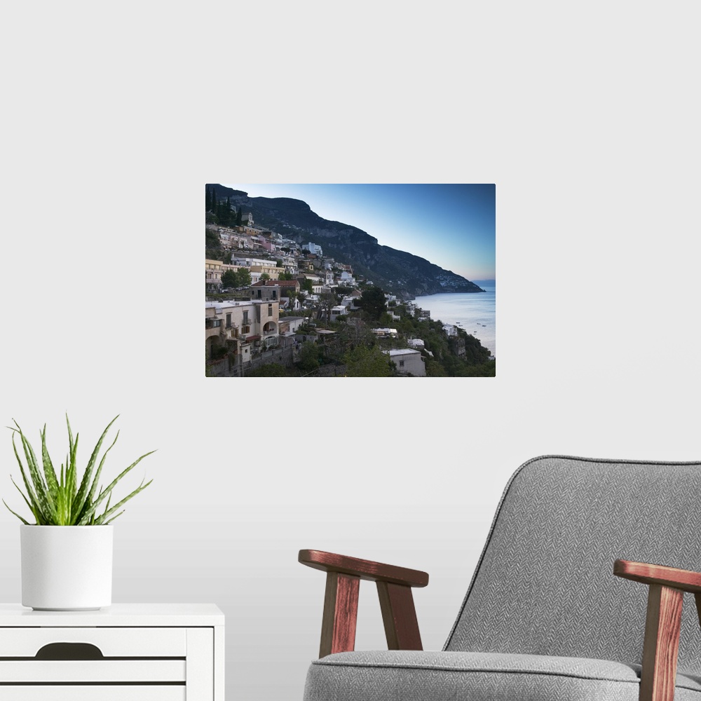 A modern room featuring Oversized artwork that is a picture of a town on a coast in Italy. A large hill is seen in the di...