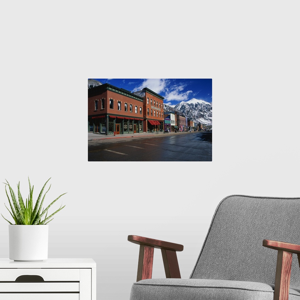 A modern room featuring Photograph of street corner lined with buildings and shops with snow covered mountains in the bac...