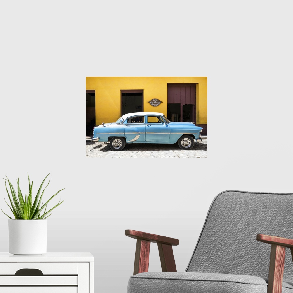 A modern room featuring Photograph of a blue vintage car parked in front of a bright yellow building on a cobblestone road.