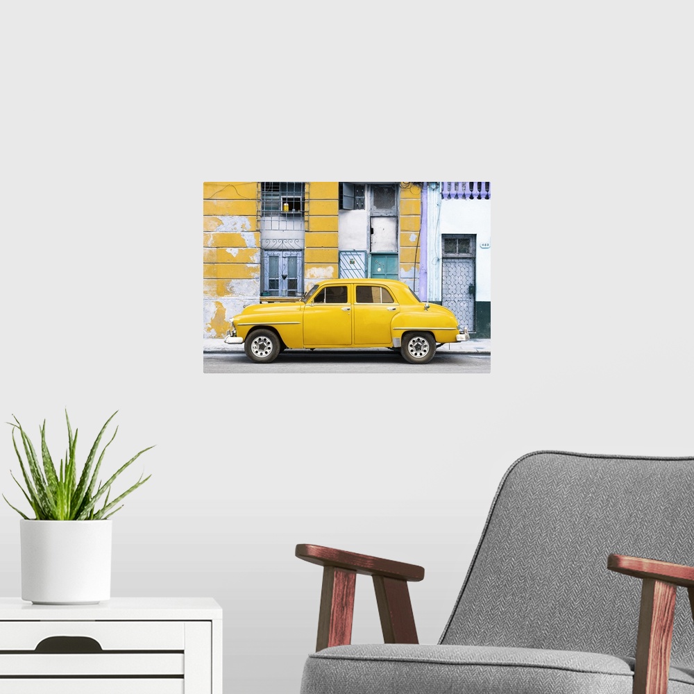 A modern room featuring Photograph of a yellow vintage car parked on the side of a street with an old building in the bac...
