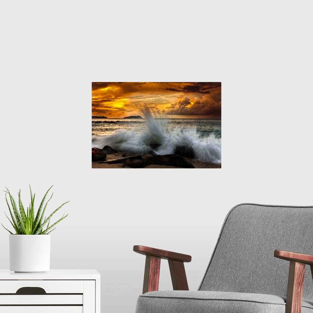 A modern room featuring Waves crashing on the rocky shore at sunset.