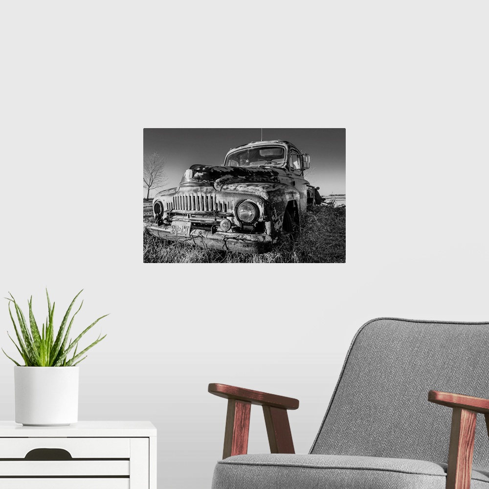 A modern room featuring A black and white image of an old pick-up truck slowly sinking in the grass of an old farm yard a...