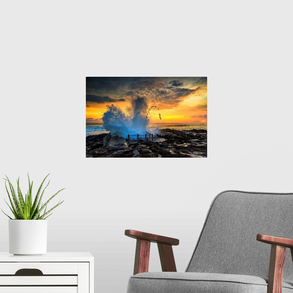 A modern room featuring Waves crashing onto the rocky shore at sunset.