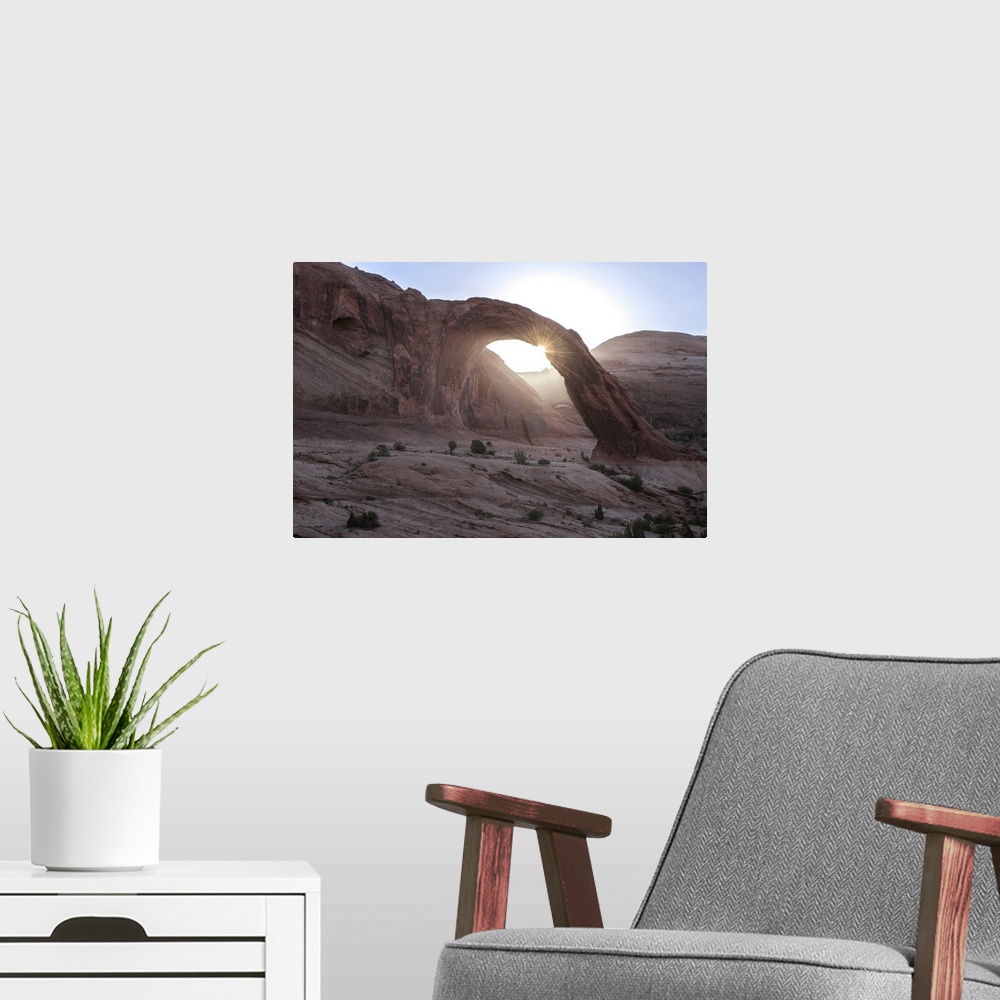 A modern room featuring The sun peeking behind the Corona Arch with a view of the desert landscape in Arches National Par...