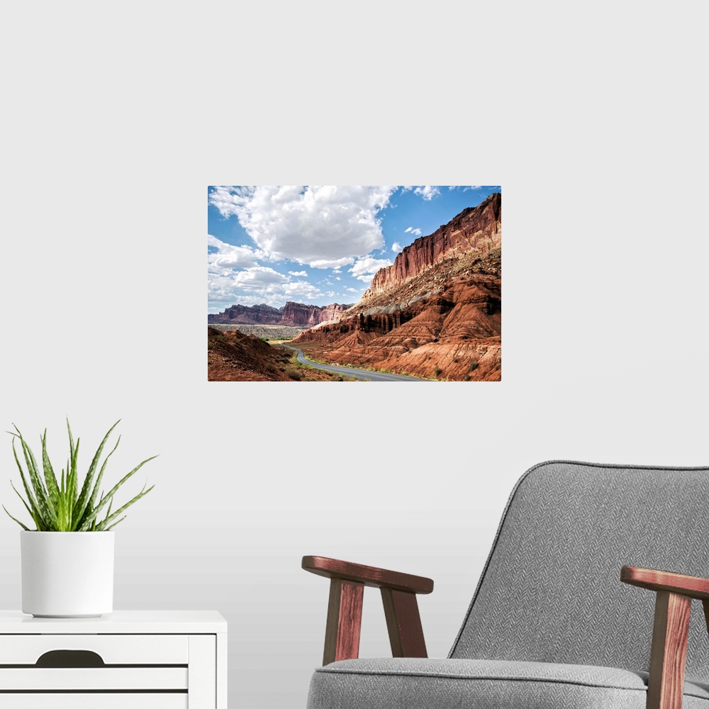 A modern room featuring A road winds through Capitol Reef National Park while puffy clouds scatter across a bright blue sky.