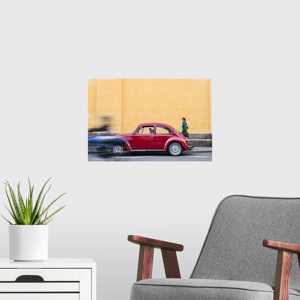 A modern room featuring A woman walking past a red VW Beetle in the colourful streets of Popayan, Colombia, South America