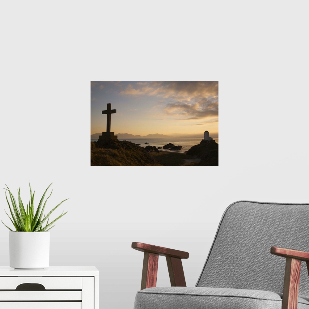 A modern room featuring Stone Cross and old lighthouse in silhouette at sunset, Anglesey, North Wales, UK