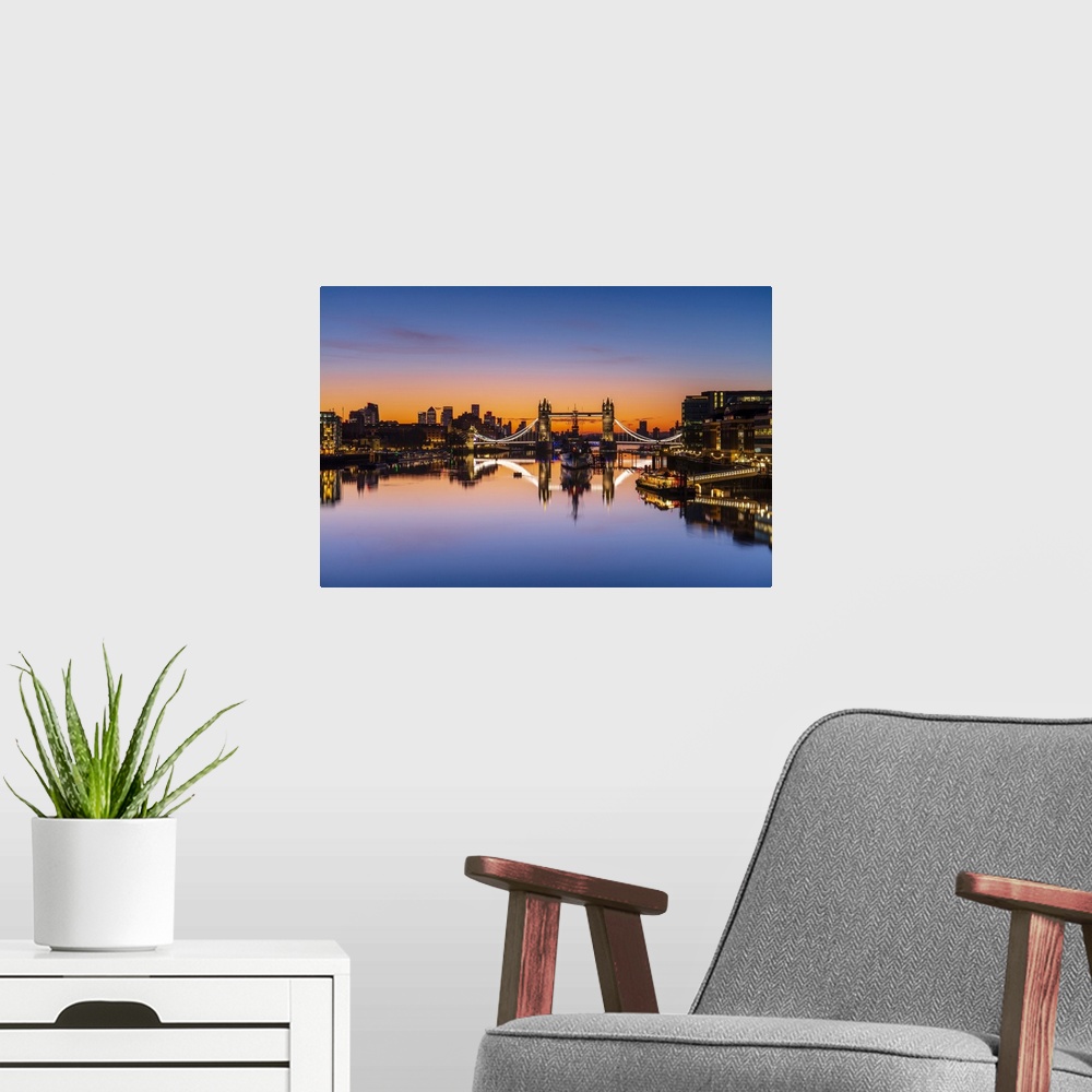 A modern room featuring Tower Bridge, HMS Belfast and reflections in a still River Thames at sunrise, London, England, Un...