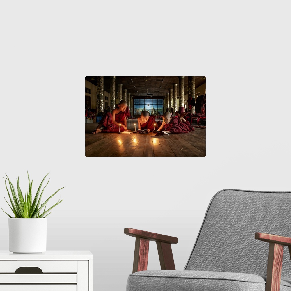 A modern room featuring Burmese monks reading by candlelight in their monastery