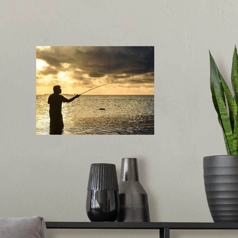 A modern room featuring A silhouetted man fly fishing on the beach in Belize at sunset.