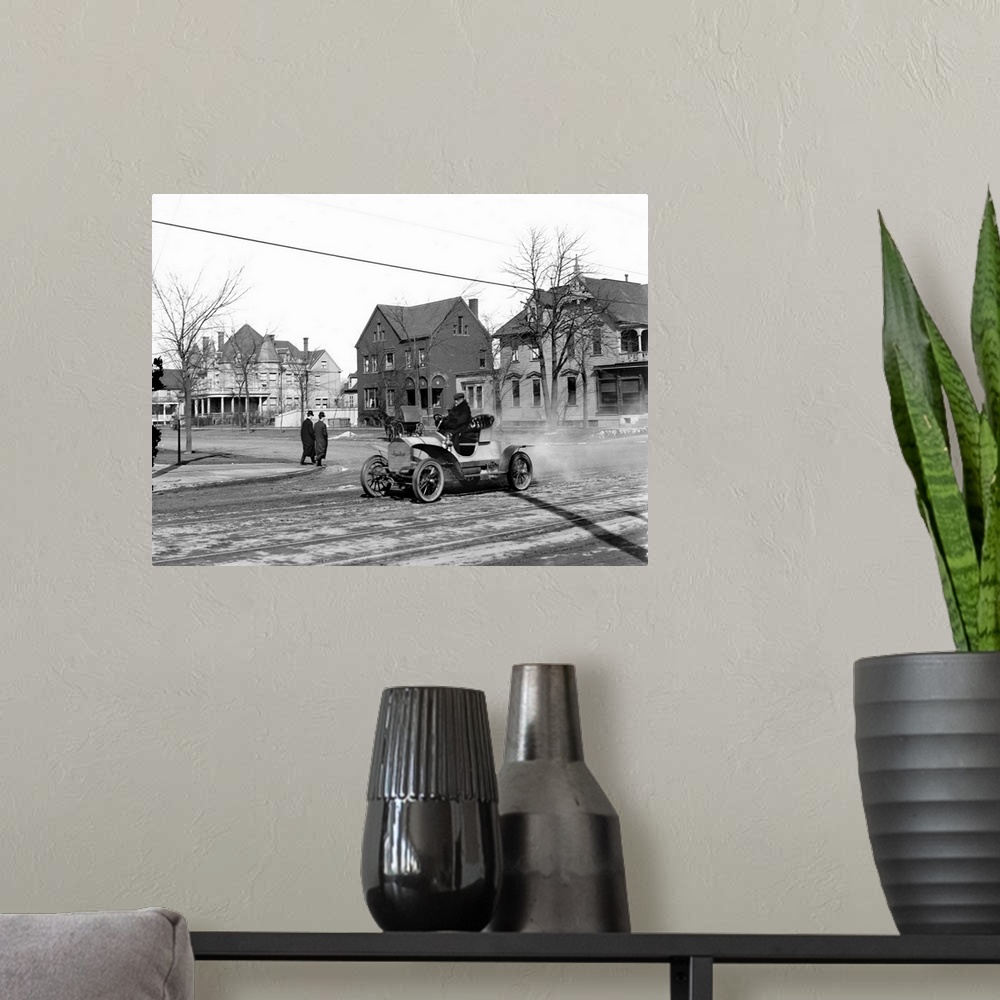 A modern room featuring Man driving an automobile through an American town. Photograph, c1905.