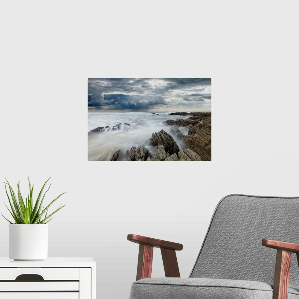 A modern room featuring Jagged rocks on coastline with white surf under grey storm clouds