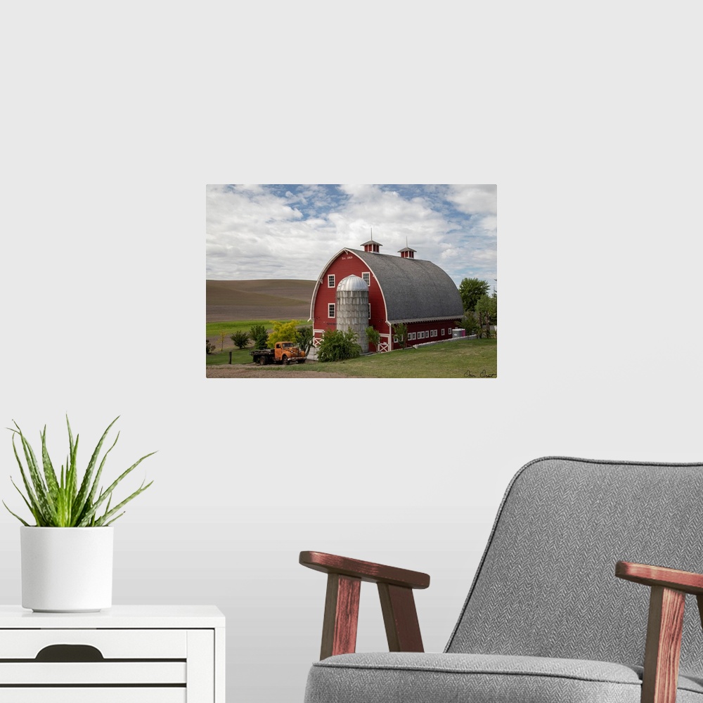 A modern room featuring A photograph of a large red barn and grain silo with a vintage orange truck parked out front