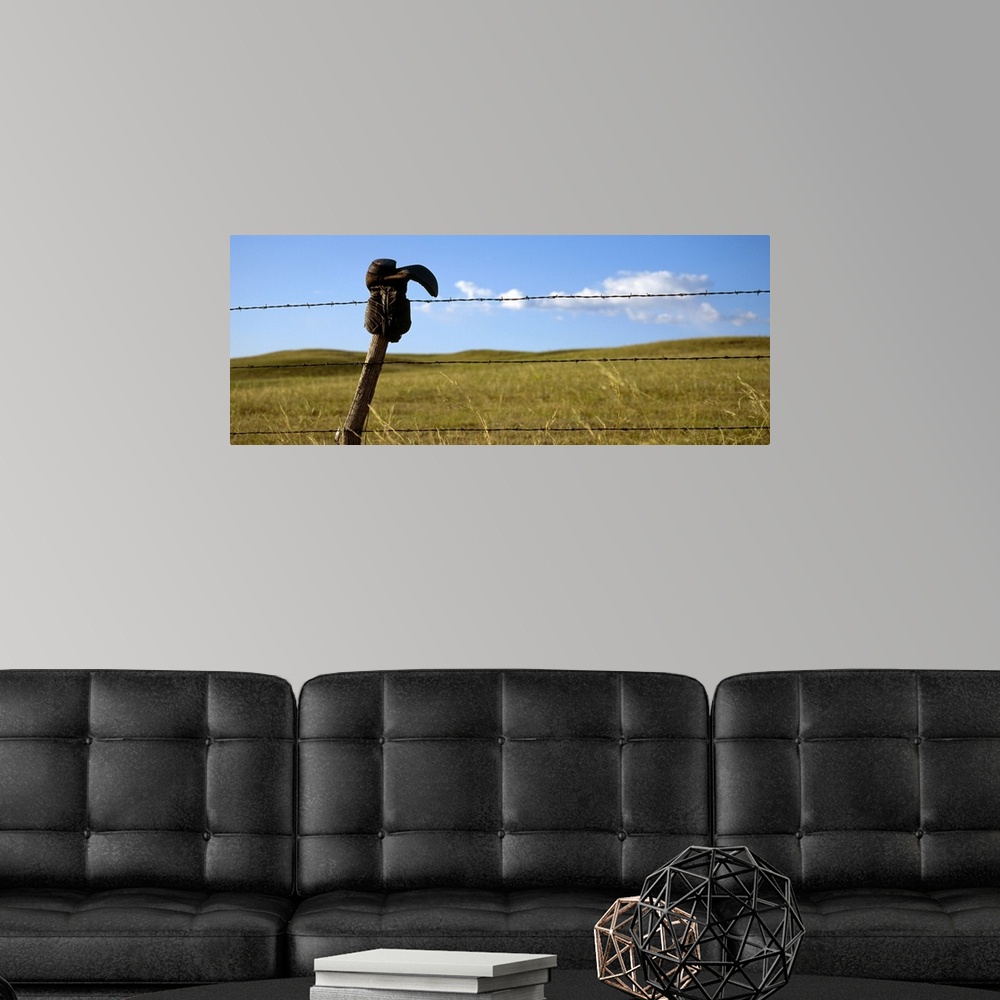 A modern room featuring Panoramic photograph of cowboy boot hanging upside down on a cable fence with grass covered hills...