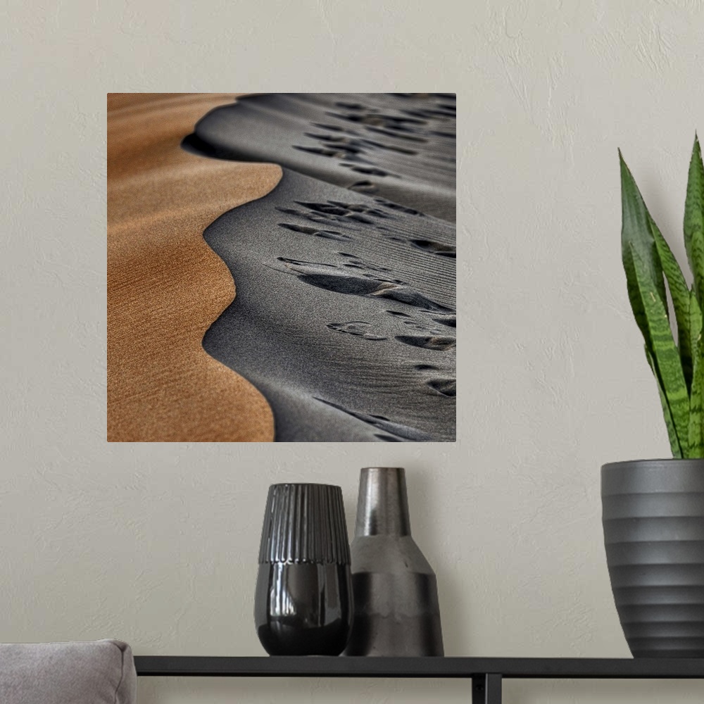 A modern room featuring Two opposing sides of a sand dune, one smooth and orange, the other grey and full of footprints.