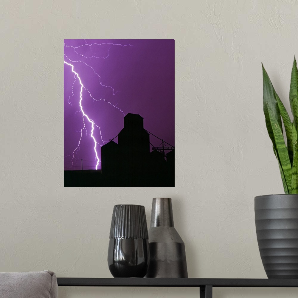 A modern room featuring A bolt of lightning lights up the night sky during a storm silhouetting a grain elevator