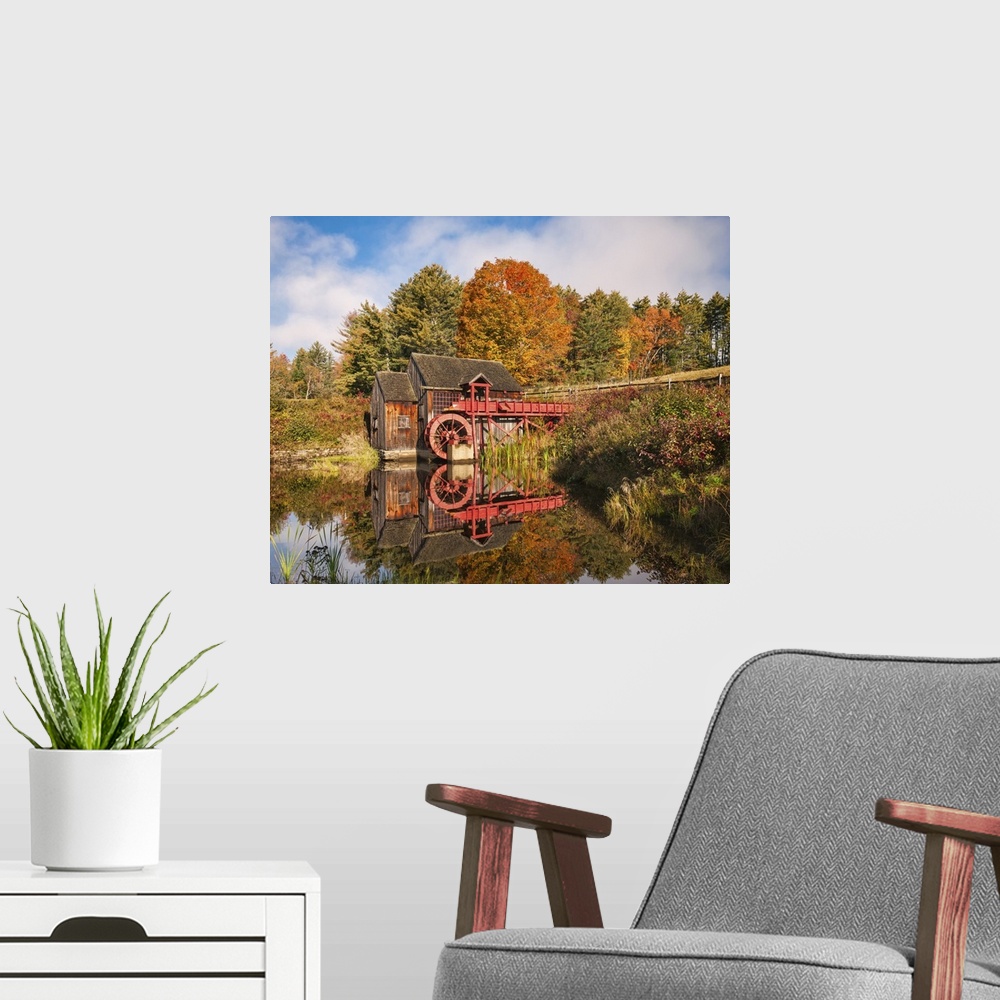 A modern room featuring A photograph of a red water mill in the middle of a forest in autumn foliage.