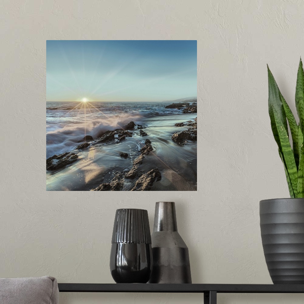 A modern room featuring Square photograph of ocean waves crashing on a rocky shore with the sun setting on the horizon li...