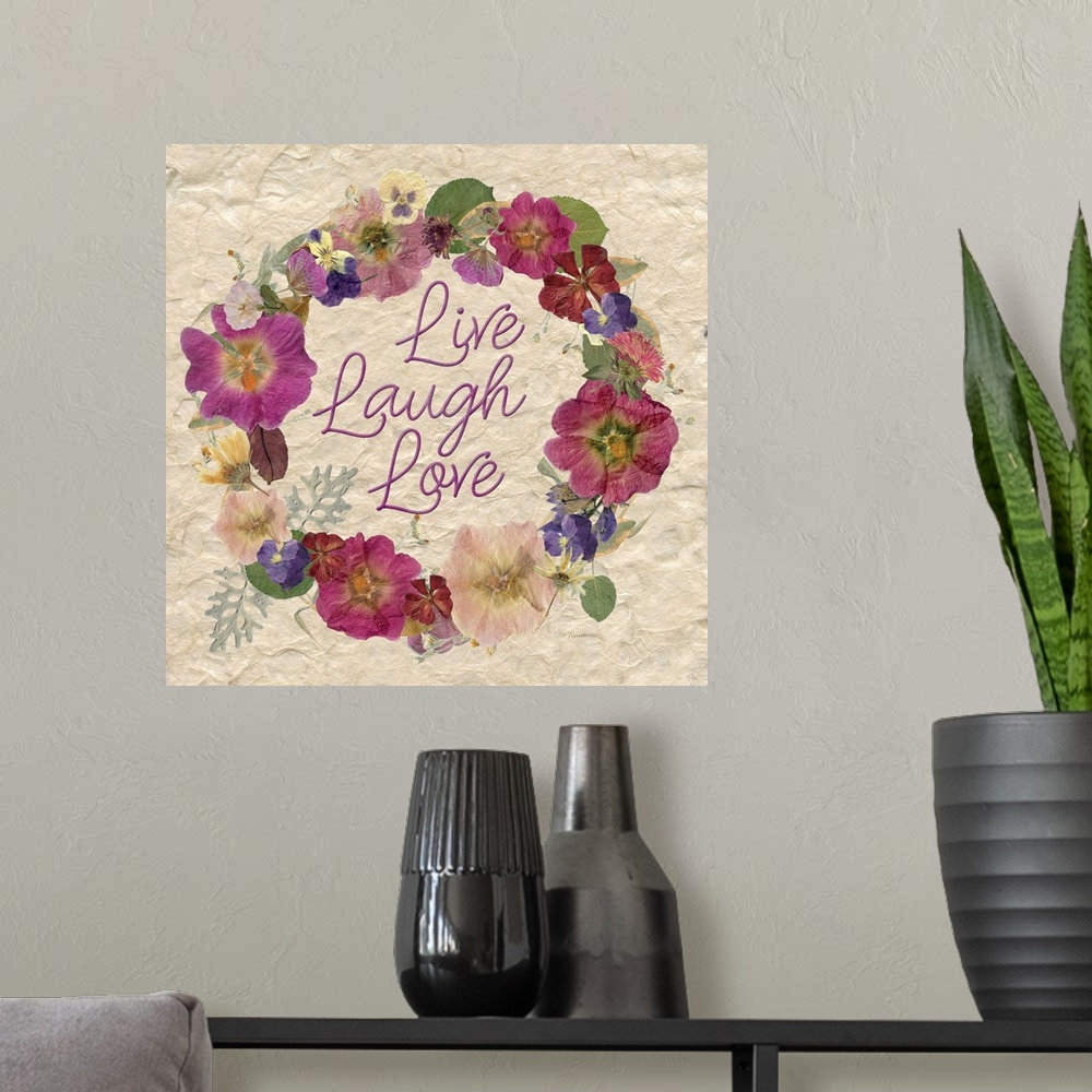 A modern room featuring A wreath of various dried flowers and foliage surround the words, "Live, laugh, love" on a natura...