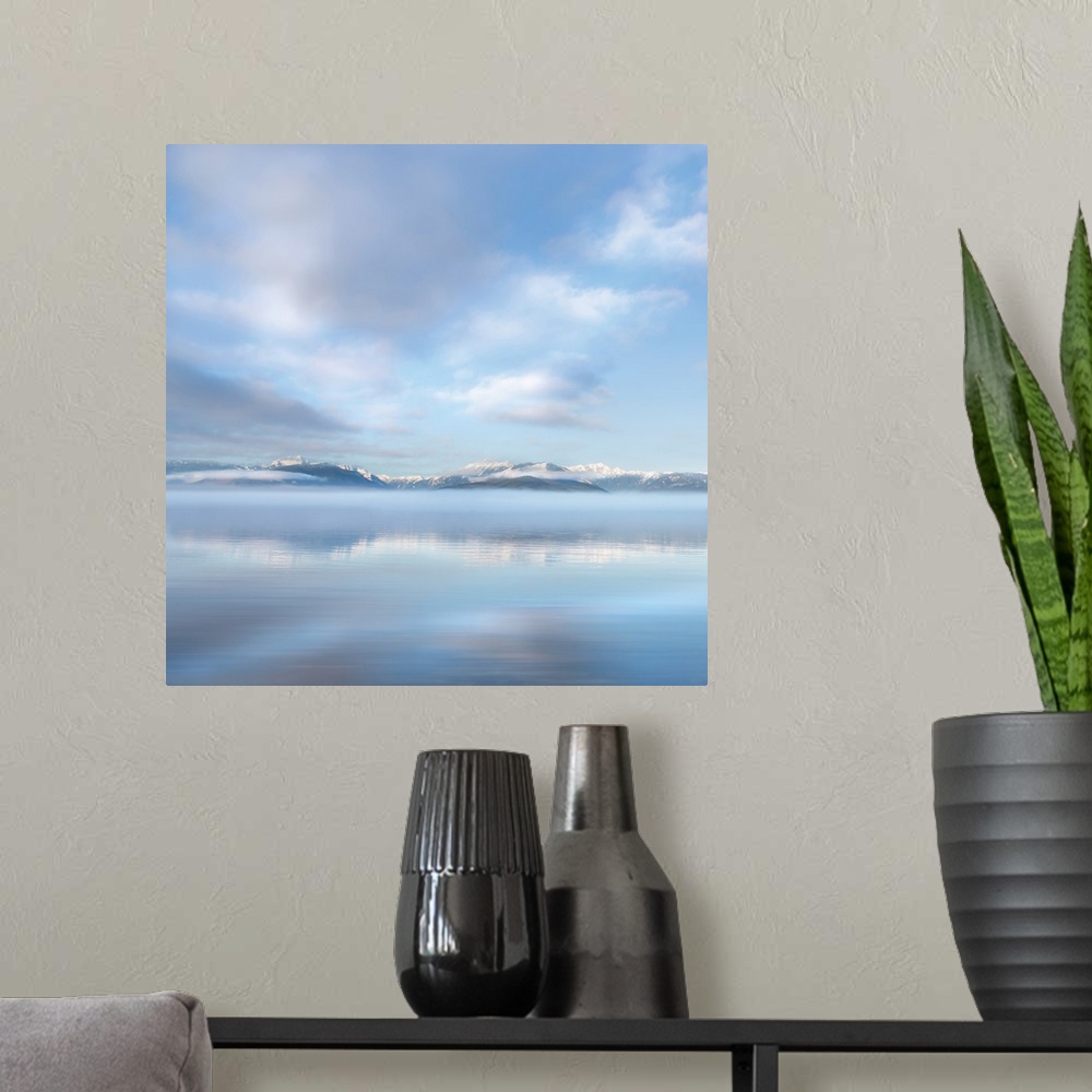 A modern room featuring Square photograph of a snow capped mountain range in the distance with fluffy clouds above reflec...