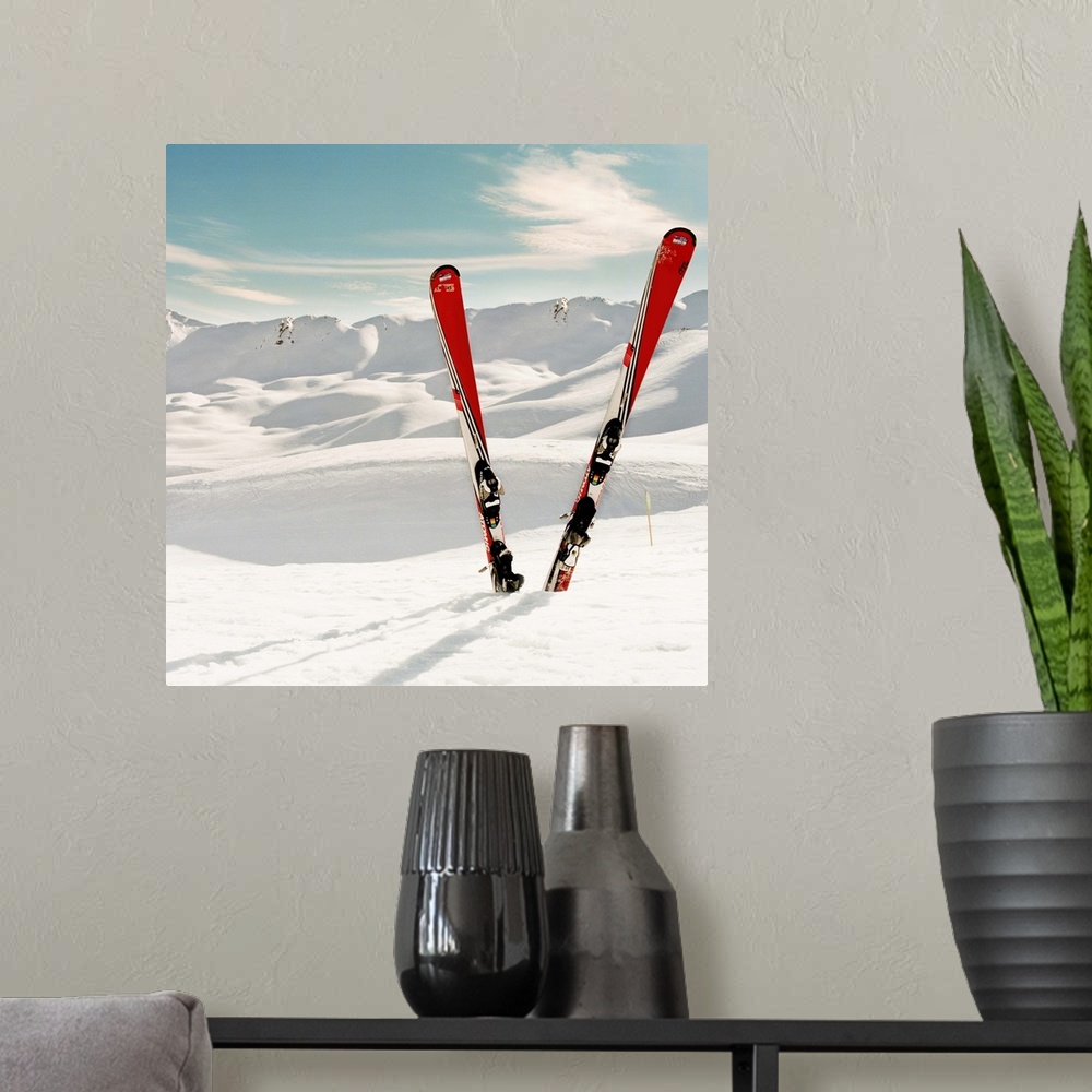 A modern room featuring Red pair of ski standing in snow.Mountains in background