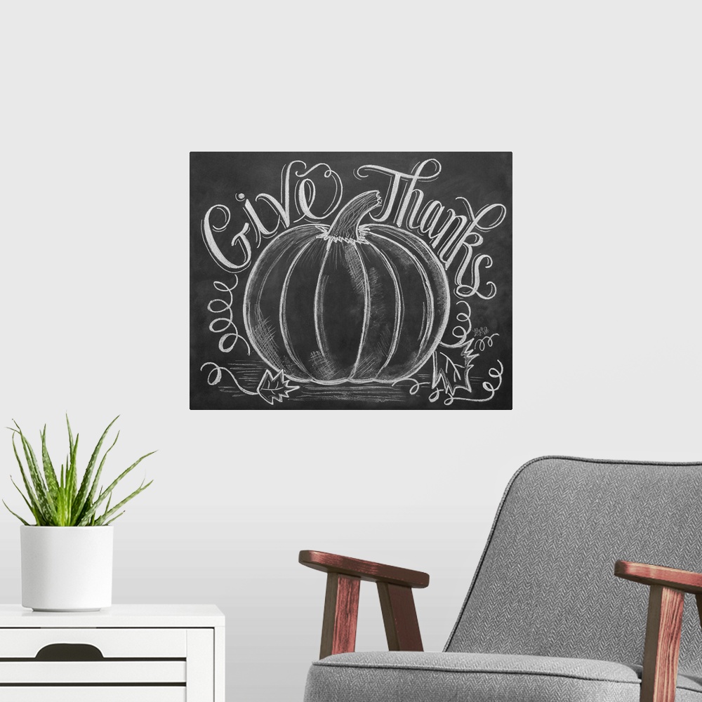 A modern room featuring "Give Thanks" handwritten with a drawing of a large pumpkin in white chalk on a black background.