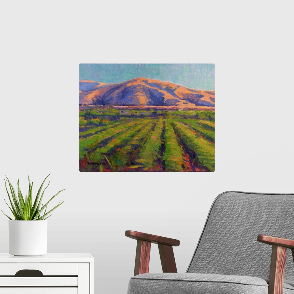 A modern room featuring A contemporary painting of fields with mountains in the background.