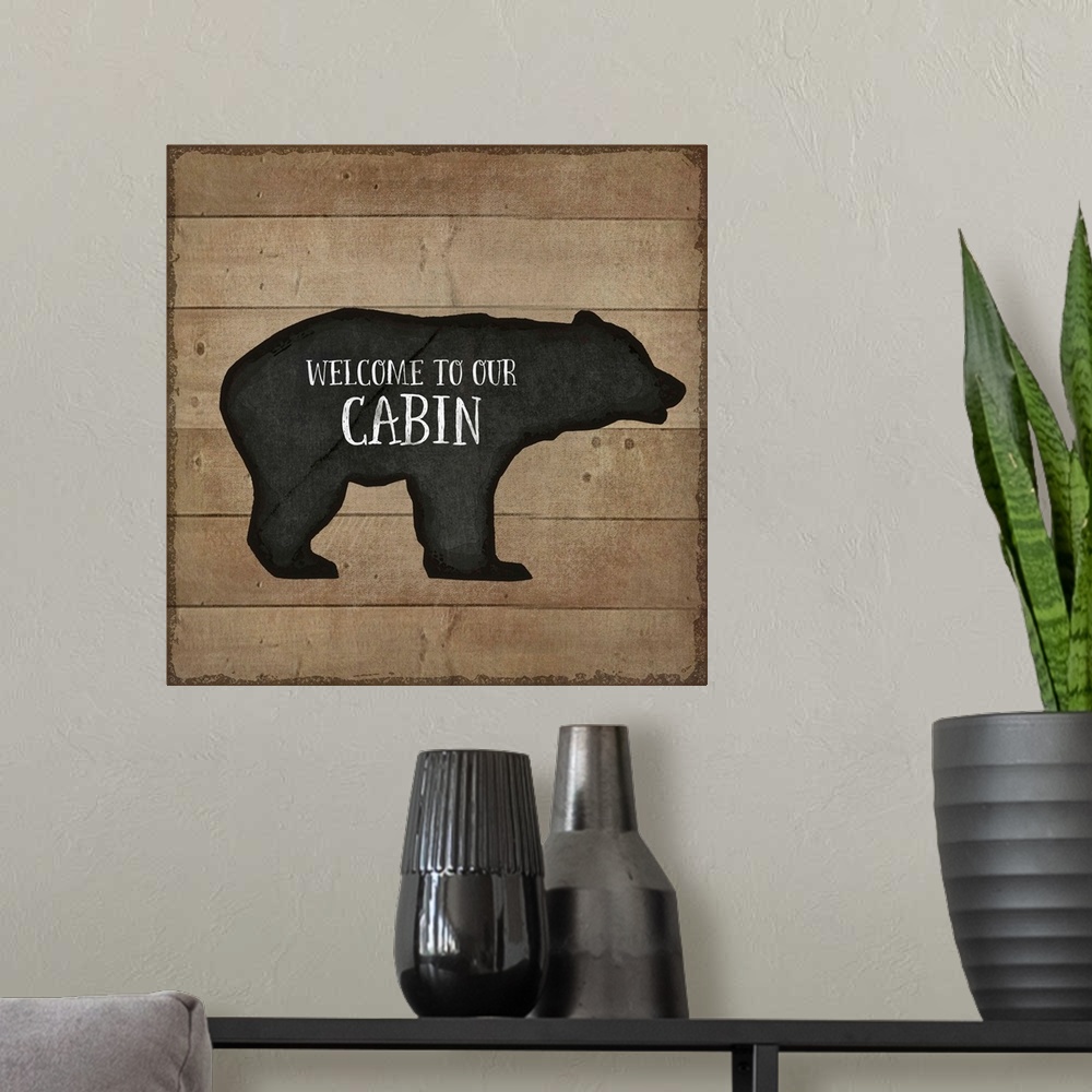A modern room featuring "Welcome to Our Cabin" on a bear silhouette over a wooden background.