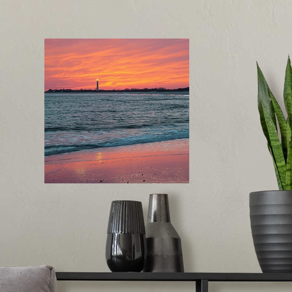A modern room featuring Vivid orange sunset sky over the ocean at low tide, with Cape May lighthouse shining in the dista...