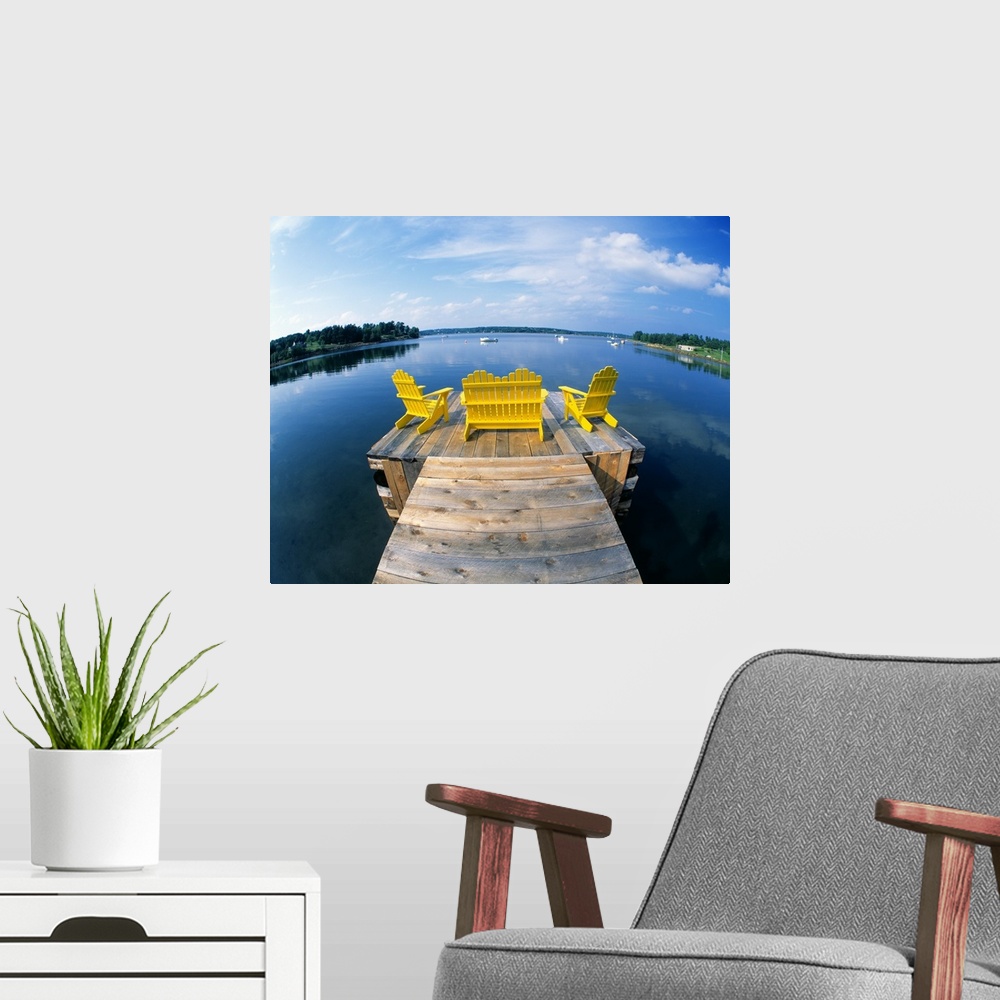 A modern room featuring Outdoor wooden chairs sit at the end of a small dock and look out onto a large body of water.