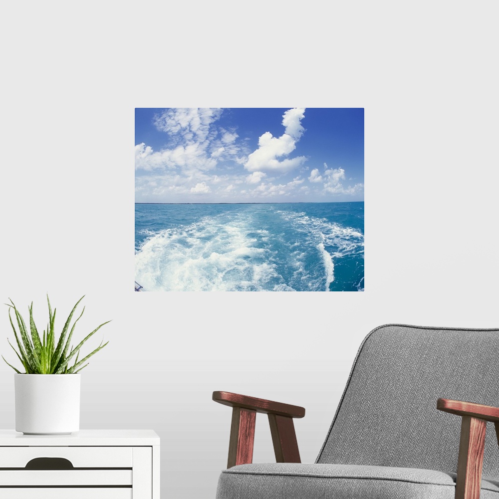 A modern room featuring Photo on canvas of the ocean with land in the far distance and puffy clouds above looking from be...