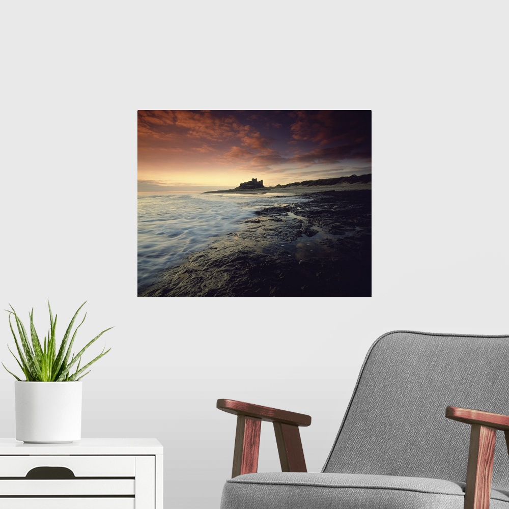 A modern room featuring Oversized landscape photograph of a rocky shoreline in England at sunset, Bam burgh Castle can be...