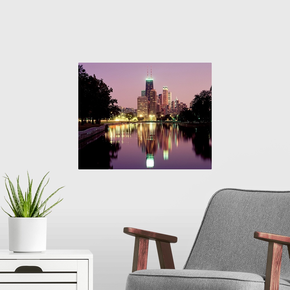 A modern room featuring Oversized photograph wall art of city lights and skyscrapers reflecting in a pond in a park.